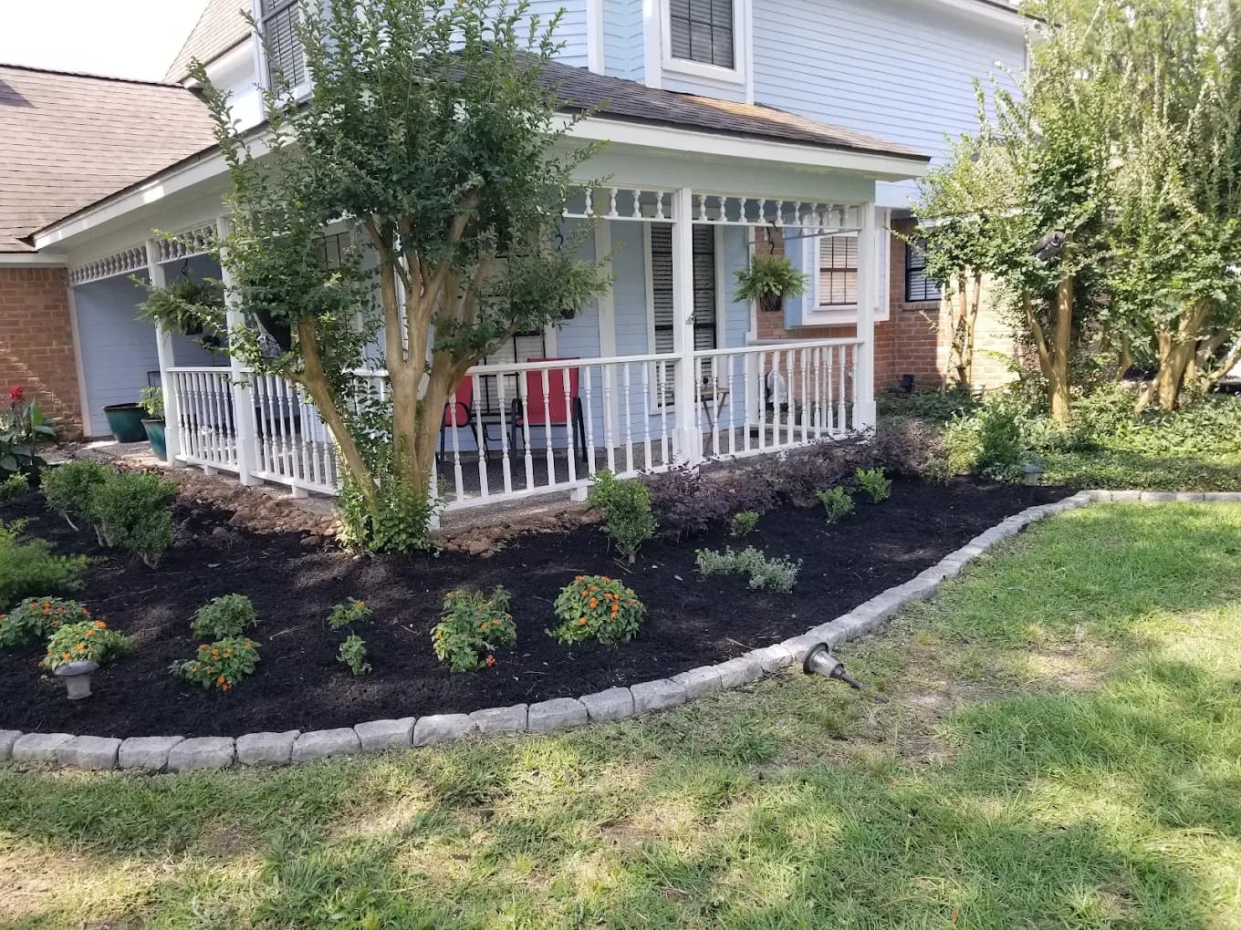 Fresh dark mulch beds and new shrubs framing a white-porch Houston home landscaped by Seventree